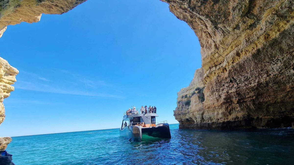 Catamaran cruising below the ochre cliffs between Albufeira and Benagil on a coastline boat tour, a relaxed option among things to do in Albufeira, Algarve